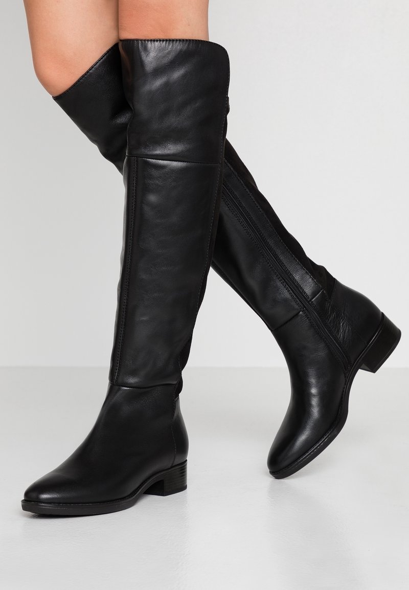 Botas de cuero negras hasta la rodilla con una textura suave, que cuentan con una cremallera lateral, un tacón bajo y una silueta ajustada.