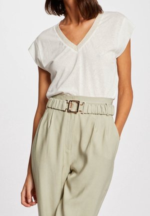 Mujer que lleva una camiseta blanca de cuello en V y manga corta metida dentro de unos pantalones beige de tiro alto con un cinturón a juego y una hebilla dorada.