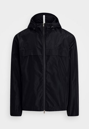 Melnā vieglā ar rāvējslēdzēju aizdares jaka ar kapuci, kurai ir gluda tekstūra, aukliņu akcenti un priekšējā krūšu kabatas dizains.