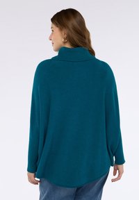 Maglione oversize color teal con collo alto, maniche a coste e orlo curvo. Realizzato in morbido materiale lavorato a maglia, presenta una silhouette rilassata.