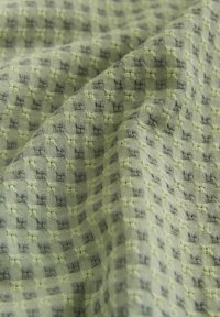 Audums ar ģeometrisku rakstu gaisā zaļā un pelēkā krāsā. Šis audums ir teksturēts, radot vizuāli pievilcīgu šaha dizainu.