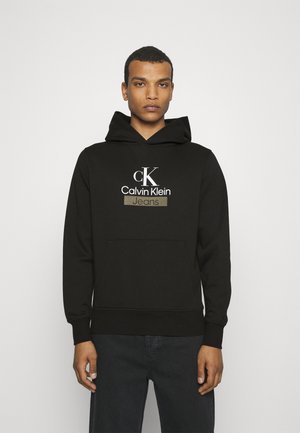 Felpa nera in cotone, dotata di una grande tasca frontale, cappuccio con cordino e logo ricamato Calvin Klein Jeans in colori a contrasto.