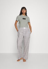 Camiseta de manga corta, de color verde claro, con un logo negro en el pecho, combinada con pantalones sueltos de cuadros grises que cuentan con una cintura elástica.