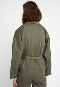 Olvihgreen belted takki, jossa on rento istuvuus, kaulus ja napilliset hihansuut, valmistettu pehmeästä puuvillamateriaalista.