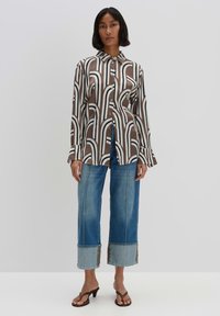 Brauner und cremefarbener Hemd mit Knöpfen und Wellenmuster, kombiniert mit hellblauen Jeans aus Denim mit ausgefranstem Saum und kontrastierender Borte.