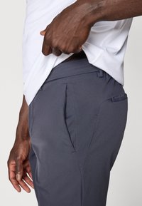 Pantalones grises a medida con bolsillos laterales, que presentan una textura suave y un diseño estilizado. La cintura se sitúa justo por encima de las caderas.