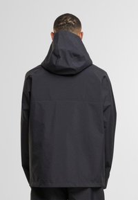 Giacca con cappuccio nera, dal tessuto leggero e liscio. Caratterizzata da una vestibilità rilassata e un design semplice, senza loghi o disegni visibili.