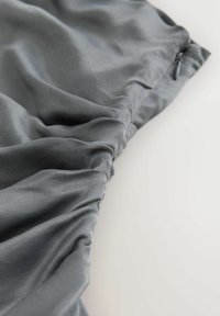 Grå elastisk stof med samlet syningdetalje på en glat overflade, der fremhæver tekstur og folder.