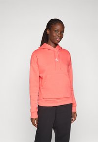 Korallrosa hoodie med en frontficka, ribbade ärmslut och en justerbar dragkedja i huvan. Har en liten vit logotyp på bröstet.