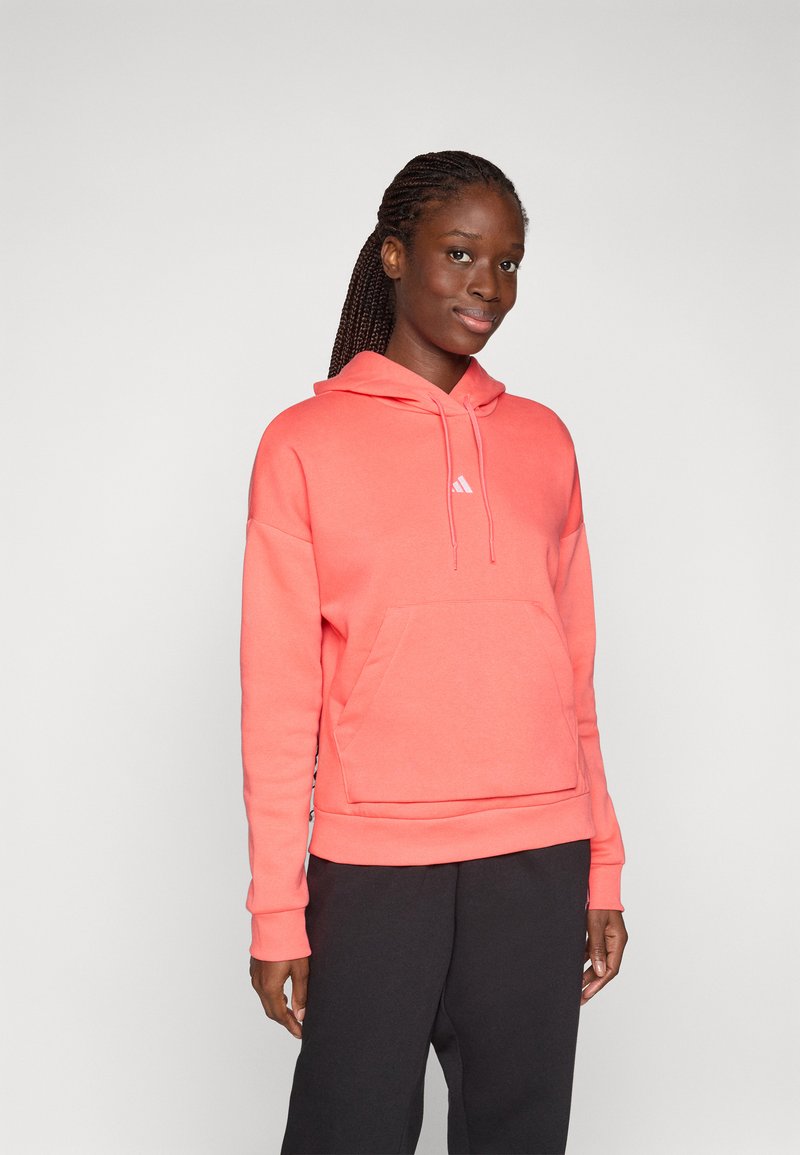 Korallrosa hoodie med en frontficka, ribbade ärmslut och en justerbar dragkedja i huvan. Har en liten vit logotyp på bröstet.