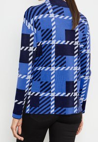 Sweter dzianinowy z niebiesko-granatowym wzorem w kratę oraz ukośnymi paskami. Długie rękawy i luźny krój, teksturowany materiał.