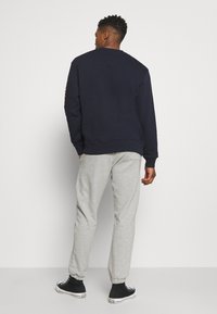 Felpa blu navy con polsini a coste indossata con pantaloni della tuta grigi. Sneakers alte nere visibili. Nessuna grafica visibile sul retro.