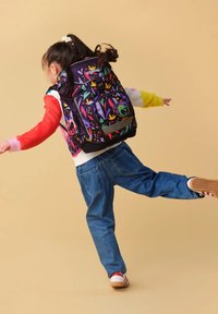 Kleurrijke kinder rugzak met bloemmotieven op een paarse achtergrond, gecombineerd met spijkerbroek en casual schoenen.
