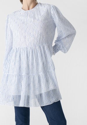 Tunique à manches longues à rayures bleues et blanches avec un ourlet volanté, réalisée en tissu léger. Elle possède des manches froncées et un col rond.