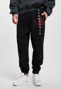 Schwarze Jogginghosen aus weichem Stoff, mit einem roten Drachenmotigraphik und weißem "DANGEROUS"-Text an der Seite, mit gerippten Knöcheln.