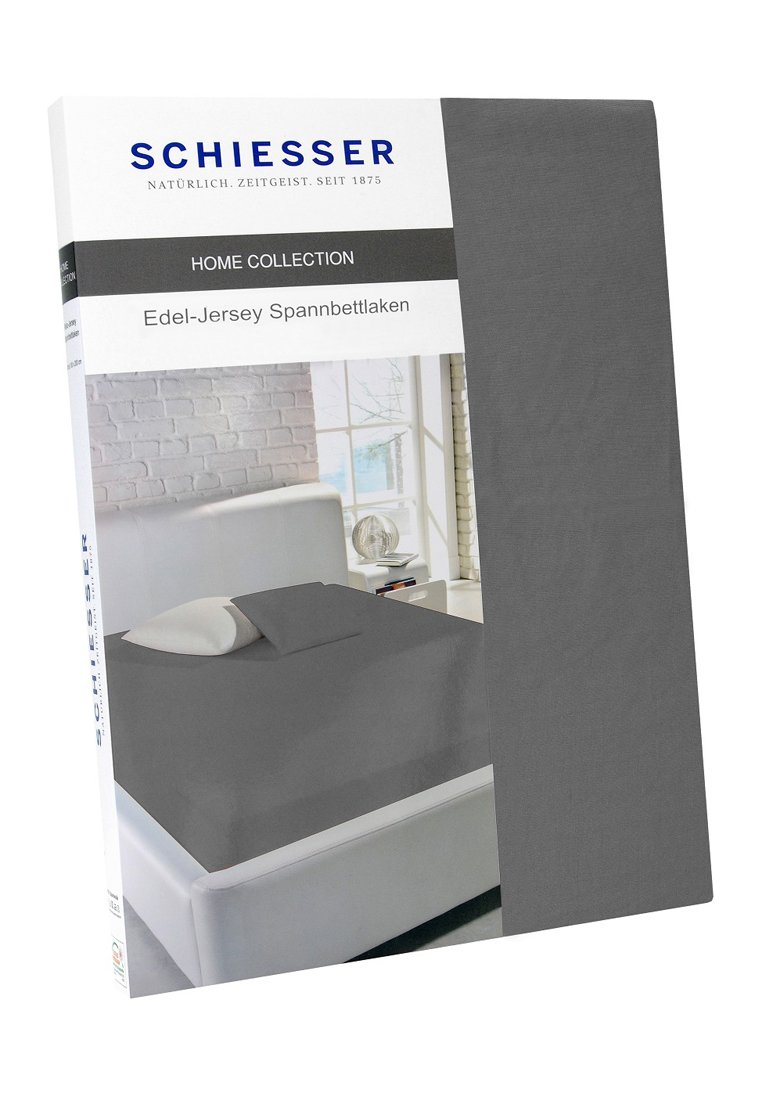 Schiesser Home Collection graue Jersey-Spannbettlaken-Verpackung, die ein Bett mit grauem Laken und Kissen in einem hellen, modernen Schlafzimmer zeigt.