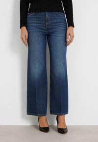 Jeans de pierna ancha en denim azul oscuro, de cintura alta con una textura suave, que cuentan con un diseño clásico de cinco bolsillos y dobladillos rectos.