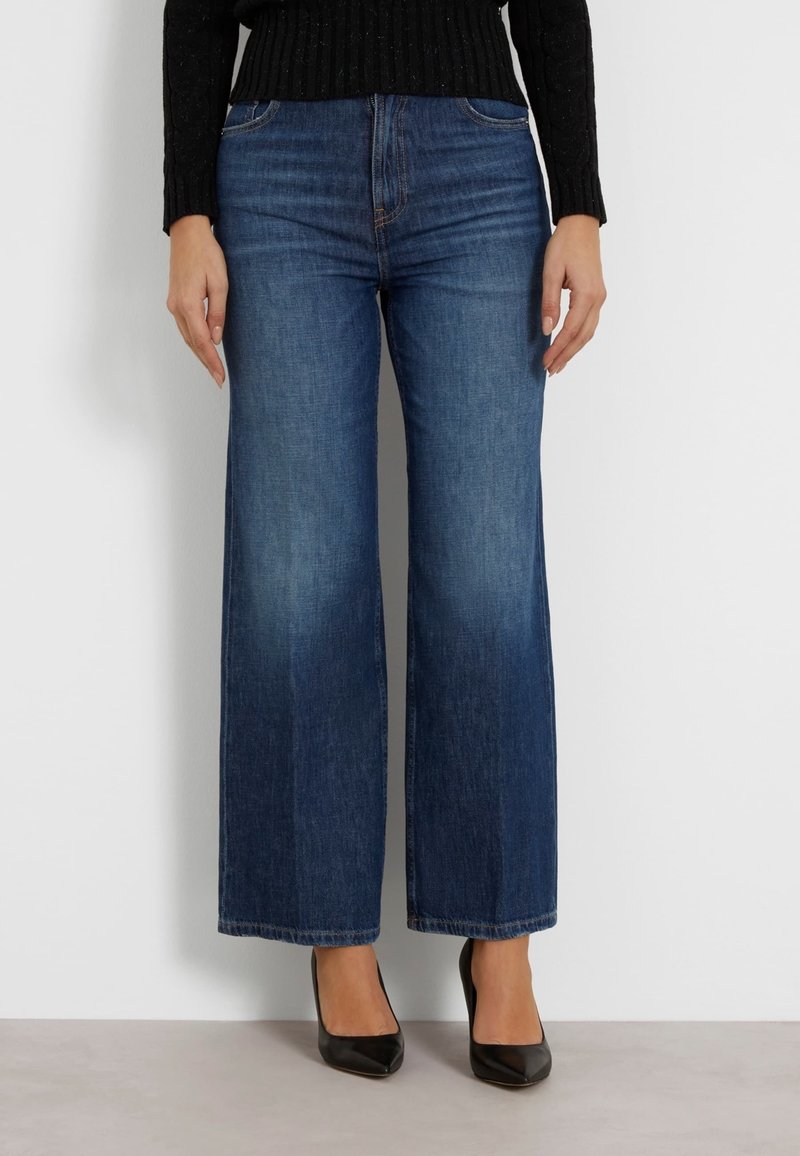 Jeans de pierna ancha en denim azul oscuro, de cintura alta con una textura suave, que cuentan con un diseño clásico de cinco bolsillos y dobladillos rectos.