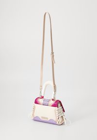 Petit sac à main en matériaux crème, rose et violet ; possède une forme structurée, des accents en dentelle et une courte poignée enroulée de tissu blanc.