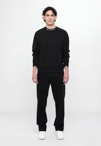 Felpa nera con scollo rotondo e polsini a costine, abbinata a pantaloni neri con cuciture bianche e sneakers bianche.