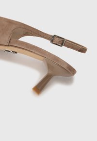 Sandaletti beige in suede con tacco alto, punta affusolata, cinturino alla caviglia, fibbia argentata e tacco a blocco trasparente con punta arrotondata.