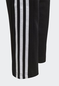 Pantalones deportivos negros con tres franjas blancas a lo largo de las costuras externas, con una textura suave y un diseño de pierna ajustada.
