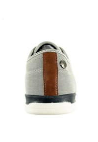 Zapatillas de lona gris de caña baja con acento de cuero marrón y detalle de logo metálico. Presenta una suela de goma en blanco y negro para mayor agarre.