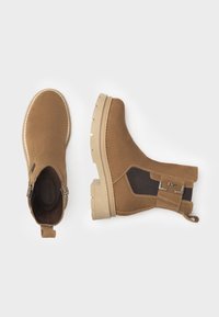Bottines en daim brun avec une semelle plate en beige texturé, des panneaux élastiques sur les côtés, des accessoires accentués et une languette à l'arrière.