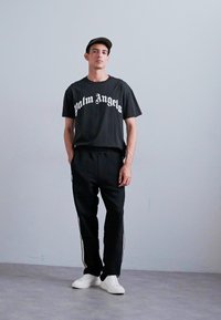Zwarte katoenen T-shirt met 'Palm Angels' logo, gecombineerd met zwarte joggingbroek met witte zijstrepen en witte sneakers.