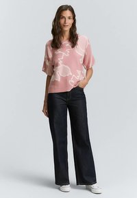 Vaaleanpunainen lyhythihainen neule, jossa valkoinen abstrakti kuvio, yhdistetty tummiin leveälahkeisiin farkkuihin ja valkoisiin tennareihin. Rentouttava istuvuus ja pehmeä materiaali.