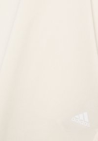 Tejido atlético blanco, textura suave, presenta líneas diagonales sutiles; incluye un pequeño logo de Adidas en blanco en la parte inferior derecha.