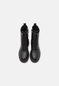 Une paire de bottines noires en cuir à lacets avec des zips latéraux et des tirettes, présentée de dessus sur un fond blanc.