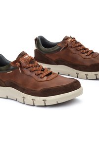 Zapatillas deportivas marrones que presentan una combinación de gamuza suave y material sintético texturizado, diseño de cordones y una suela de goma beige en contraste.