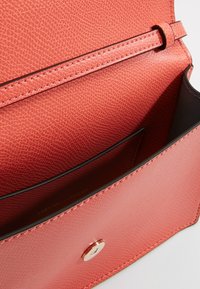 Interno della borsa in pelle a trama corallo con chiusura a scatto magnetico; presenta una fodera nera liscia in contrasto e un unico scomparto.