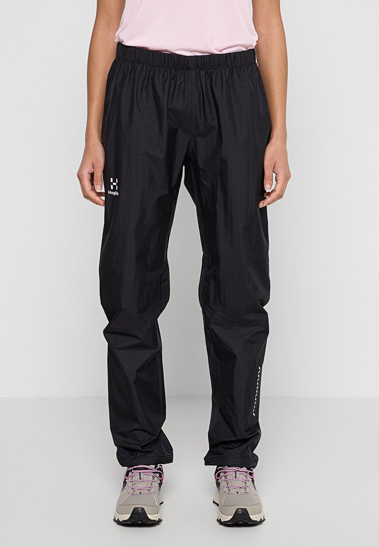 Mustat vedenpitävät housut, joissa on joustava vyötärö, kevyttä kangasta ja heijastava logo vasemmassa reidessä.