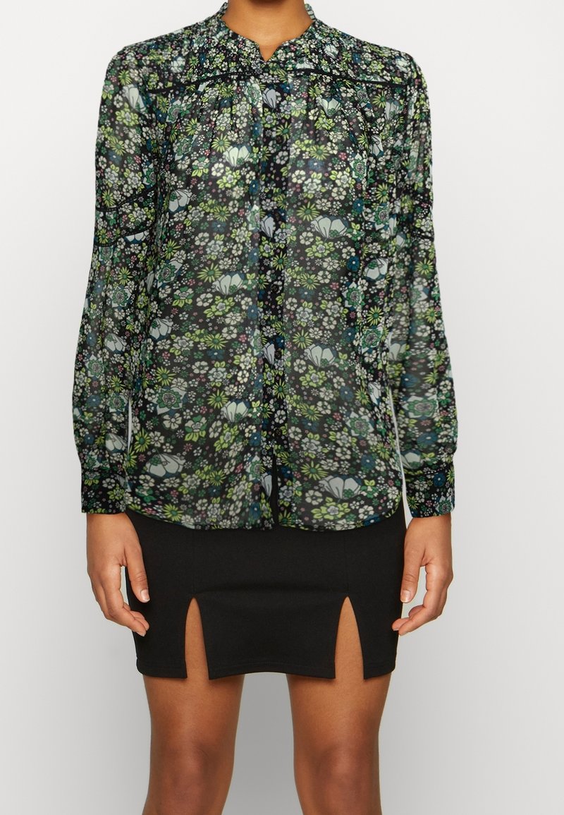 Blusa floreale in tessuto nero trasparente, con fiori multicolore, colletto stand-up e chiusura a bottoni. Abbinata a una mini gonna nera.