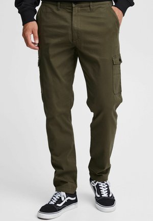 Olivengrønne cargo bukser med sidelommer, lige ben design, knaplukning og parret med sorte sneakers med hvide detaljer.