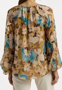 Květinová blůza s vícolor tiskem v hnědé, modré a žluté barvě. Má volný střih, měkkou tkaninu a na ramenech má řasené akcenty.