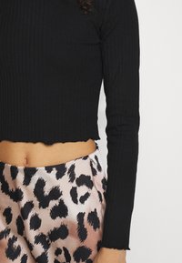 Mustassa raidoitetussa pitkähihaisessa crop-topissa on rispaantunut helma, ja se on yhdistetty satiiniseen hameeseen, jossa on vaaleanpunainen ja musta leopardikuosiset kuviot.