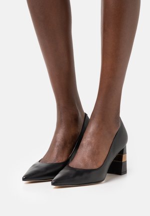 Escarpins noirs en cuir avec un design à bout pointu et un talon épais orné d'un accent doré et noir. Texture lisse, style minimaliste.