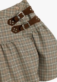 Braune und beige Hahnentritt-Rock mit zwei braunen Filzgurten mit Schnallen, silberner Hardware und einem Knopfverschluss an der Taille. Plissierter Schnitt.