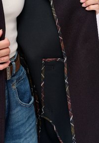 Bordeaux buitenjas met een geruite voering en een zwart binnenpaneel, met een zijzak en een gestructureerde stof.