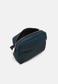 Borsa per cosmetici imbottita di colore blu navy, con zip superiore, forma piatta, tasca esterna e hardware argentato, caratterizzata da una texture liscia e resistente all'acqua.