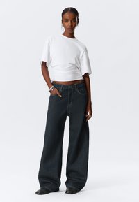 White cropped t-shirt with wide sleeves paired with high-waisted, dark blue wide-leg jeans. Model wearing black ankle boots. Minimal accessories.