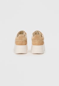 Baskets en daim beige avec une épaisse semelle blanche, présentant un bout arrondi et un col rembourré, vues de l'arrière sur fond blanc.