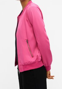 Giubbotto bomber rosa chiaro con una texture liscia, polsini a costine e tasca laterale con zip. Design semplice con una vestibilità comoda.