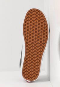 Semelle en caoutchouc d'une basket avec un motif losange et hexagone marron, une semelle intermédiaire blanche et un bord supérieur noir visible.