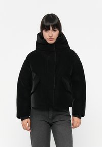 Giacca imbottita nera con collo alto, dotata di tasche laterali e una texture liscia e lucida. Il design è corto con maniche ampie.