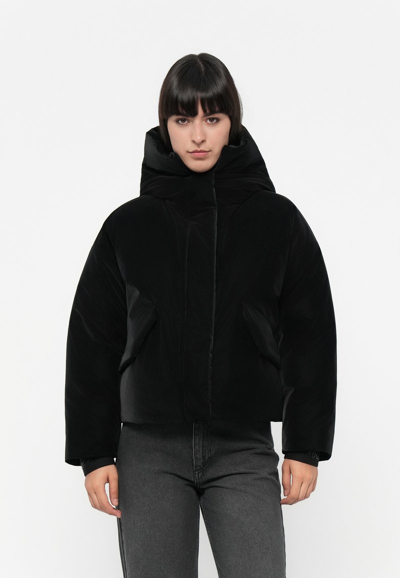 Veste noire rembourrée avec un col haut, dotée de poches latérales et d'une texture lisse et brillante. Le design est court avec de larges manches.