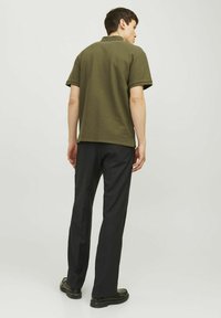 Mörk olivgrön pikétröja med korta ärmar, med en texturerad stickad design, kombinerad med svarta byxor och svarta skor.